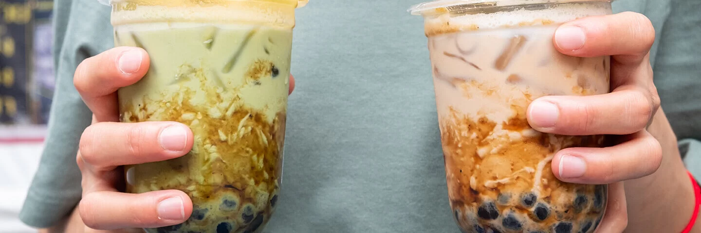 Zwei Hände tragen zwei ungesunde Bubble Tea in To-go-Bechern.