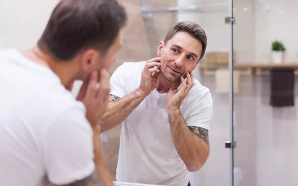 Ein Mann betrachtet seine Haut in einem Spiegel.