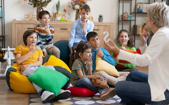 Kinder sitzen auf dem Boden oder auf Sitzsäcken und legen ihren Zeigefinger auf die Unterlippe. Mit einer Therapeutin üben sie die richtige Aussprache.
