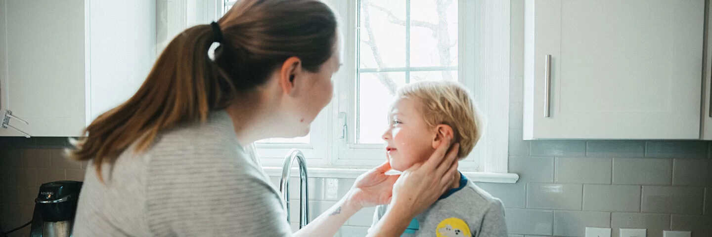 Mutter tastet jungem Sohn das schmerzende Ohr auf Mittelohrentzündung ab.