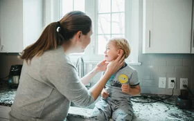 Mutter tastet jungem Sohn das schmerzende Ohr auf Mittelohrentzündung ab.