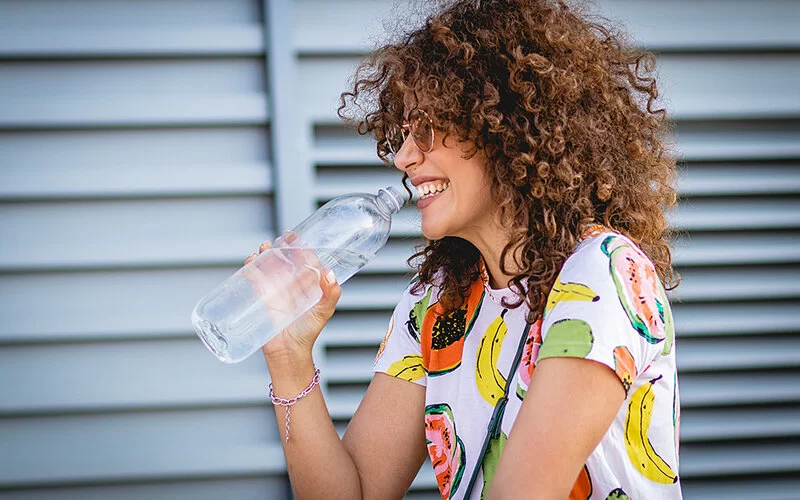 Eine junge Frau hält eine große Wasserflasche an ihren Mund, um daraus zu trinken.