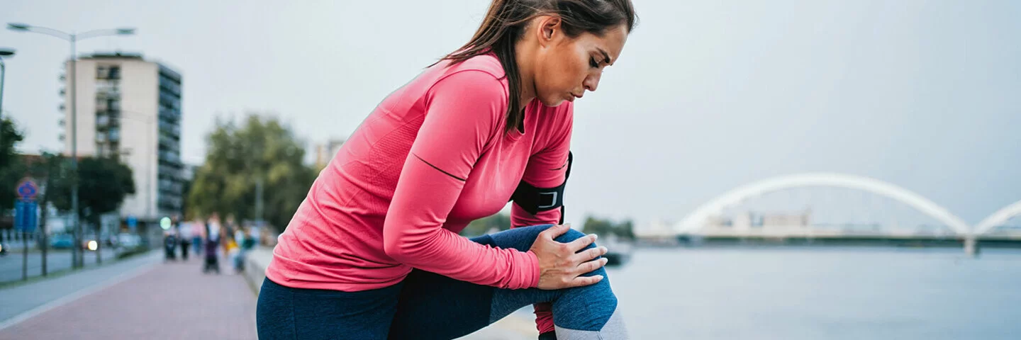 Eine Frau hält sich beim Joggen das Knie vor Schmerzen.