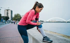 Eine Frau hält sich beim Joggen das Knie vor Schmerzen.