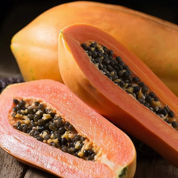 Eine ganze und eine aufgeschnittene Papaya liegen auf einem Holzbrett.