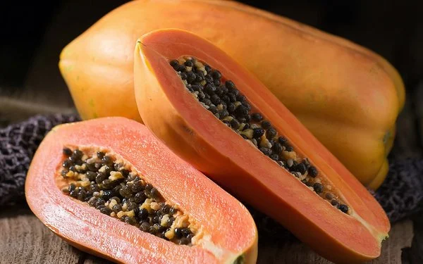 Eine ganze und eine aufgeschnittene Papaya liegen auf einem Holzbrett.