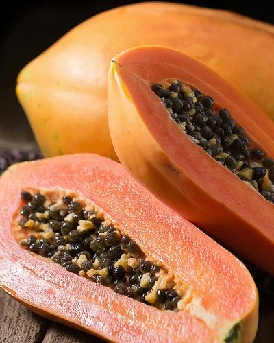 Eine ganze und eine aufgeschnittene Papaya liegen auf einem Holzbrett.