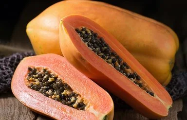 Eine ganze und eine aufgeschnittene Papaya liegen auf einem Holzbrett.