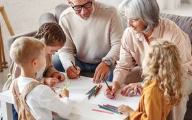 Zwei Großeltern basteln und zeichnen am Couchtisch mit ihren drei Enkelkindern.