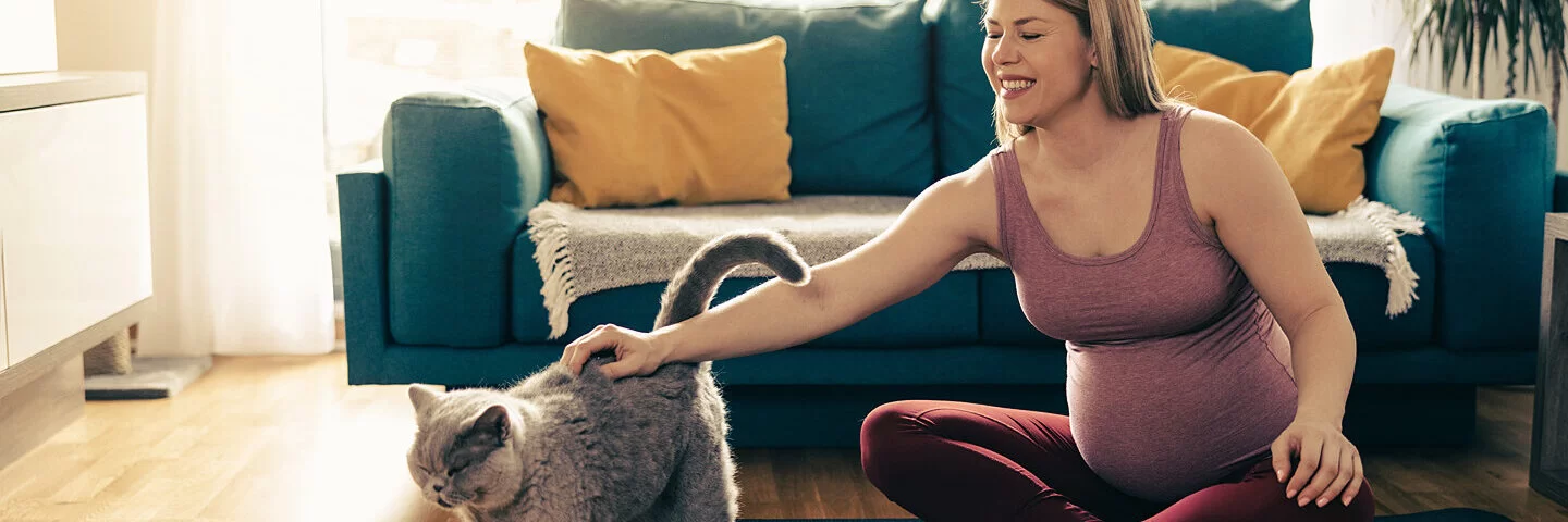 Eine schwangere Frau dehnt sich und streichelt ihre Katze.