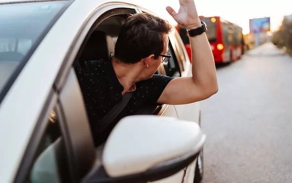 Ein Mann schaut aus einem Autofenster und hebt die linke Hand.