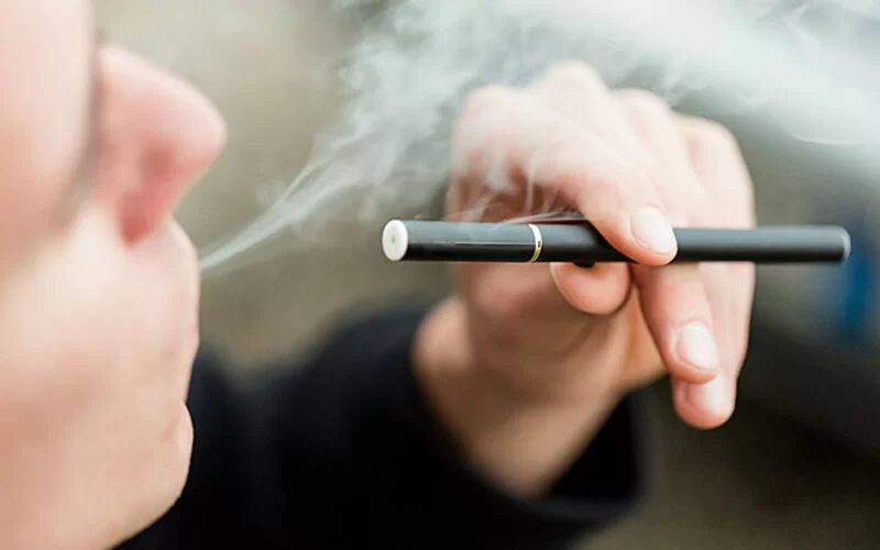 Ein Mann hält eine E-Zigarette in der Hand und bläst Rauch aus.
