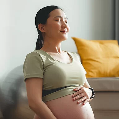 Eine junge, schwangere Frau sitzt auf dem Boden und streichelt sich über den Bauch.