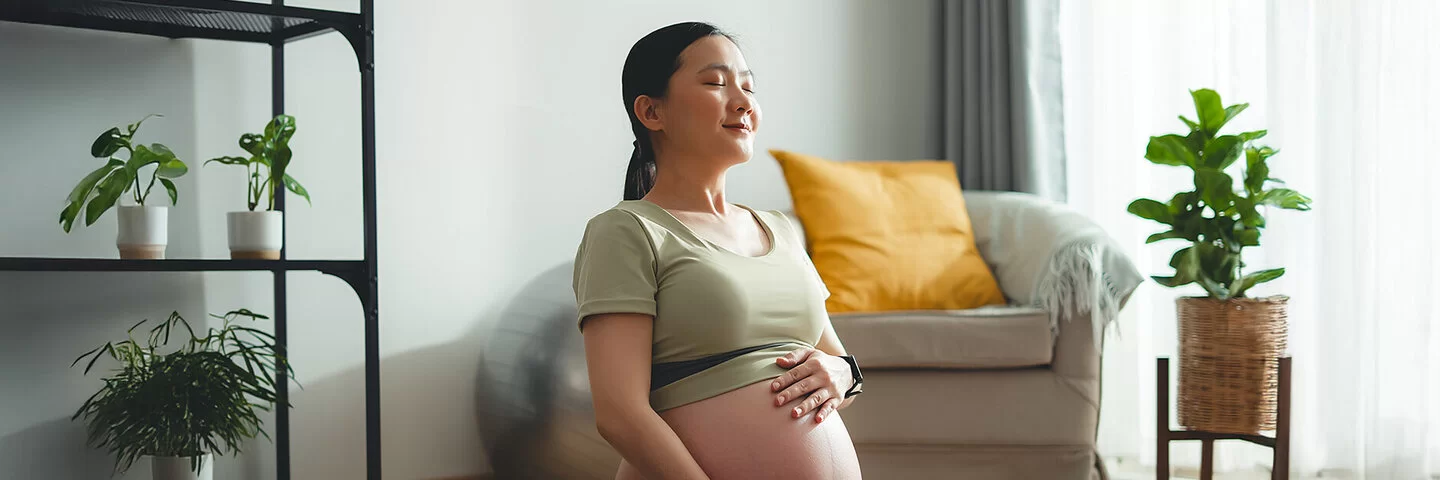 Eine junge, schwangere Frau sitzt auf dem Boden und streichelt sich über den Bauch.