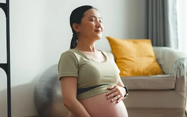 Eine junge, schwangere Frau sitzt auf dem Boden und streichelt sich über den Bauch.
