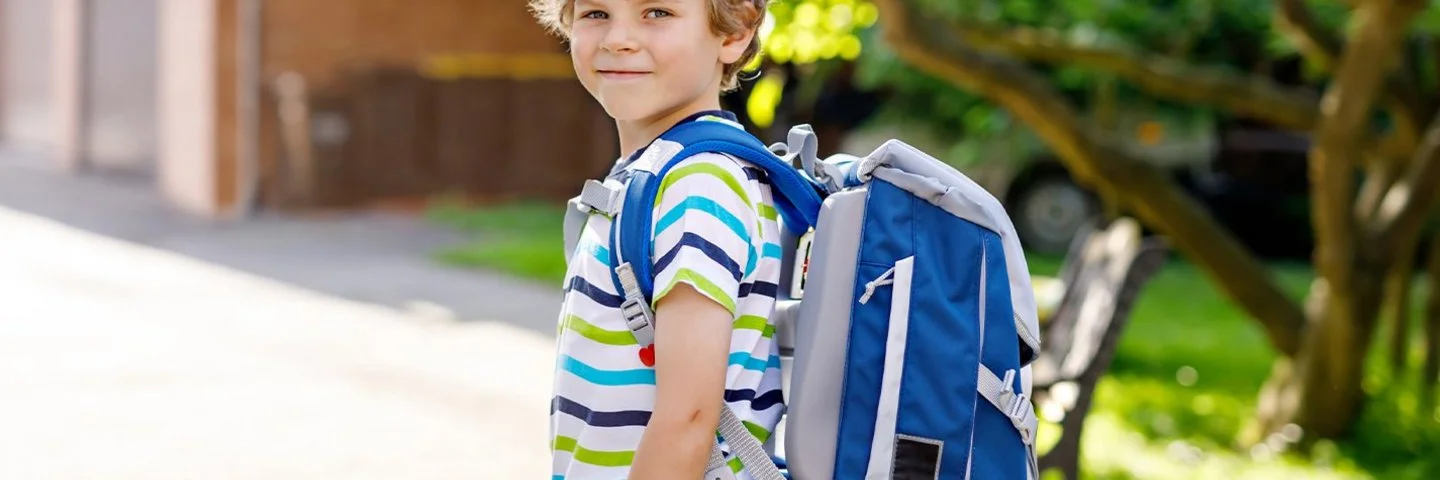 Fröhlicher Junge mit Schulranzen auf dem Weg zur Schule.