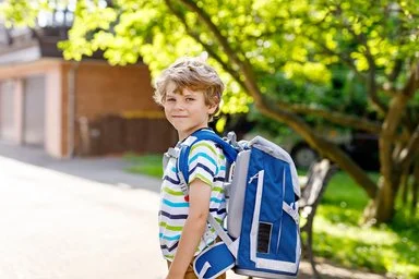 Fröhlicher Junge mit Schulranzen auf dem Weg zur Schule.