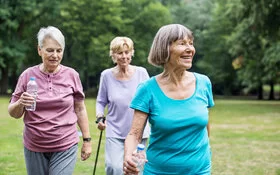 Drei Seniorinnen in Sportkleidung gehen im Park spazieren.