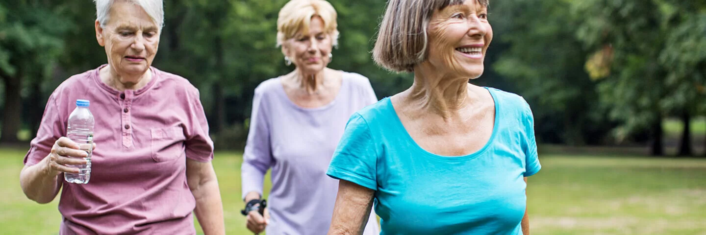 Drei Seniorinnen in Sportkleidung gehen im Park spazieren.