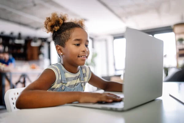 Ein Kind sitzt an einem Tisch und schaut auf den Bildschirm eines Laptops. 
