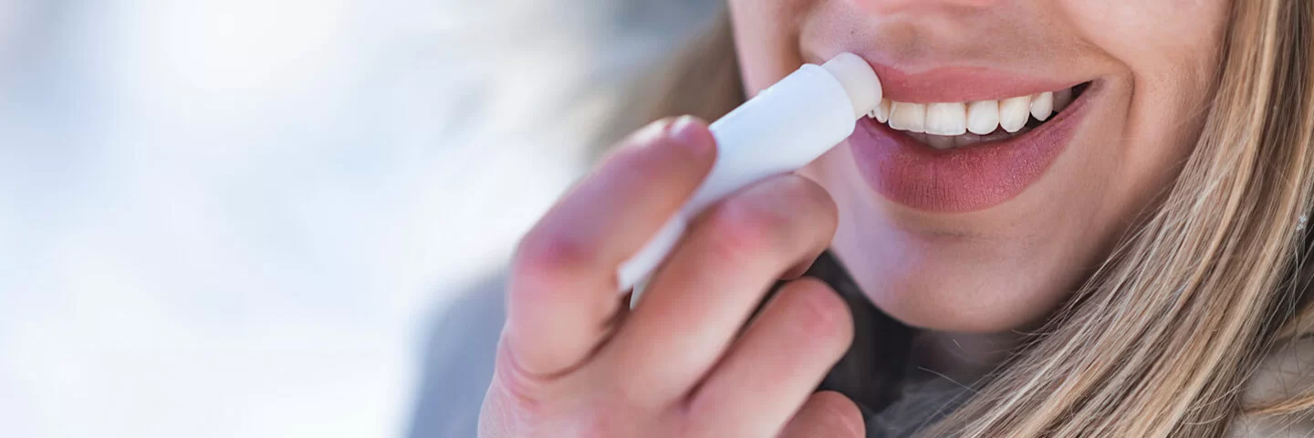 Eine Frau mit spröden Lippen pflegt ihre Lippen im Winter mit Lippenbalsam.