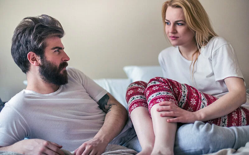Ein Mann und eine Frau sitzen im Bett und schauen sich an. Sie sprechen über Verhütung und Geschlechtskrankheiten.