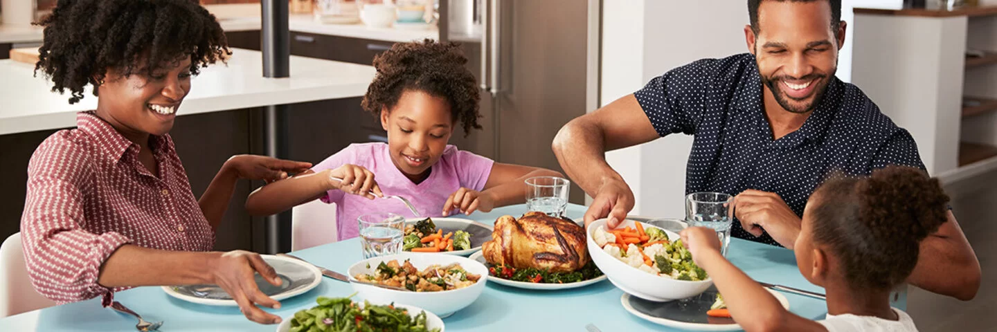 Familie sitzt am Tisch und genießt eine gemeinsame Mahlzeit in Form von Geflügel und Gemüse.