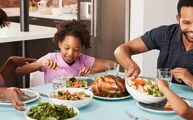 Familie sitzt am Tisch und genießt eine gemeinsame Mahlzeit in Form von Geflügel und Gemüse.