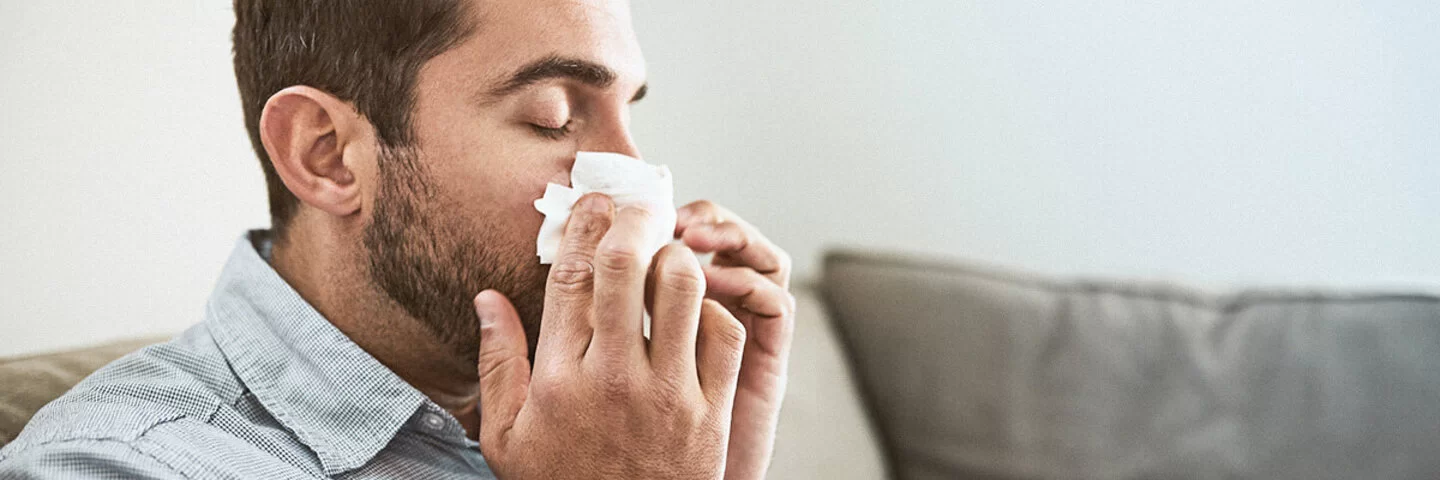 Ein Mann schnäubt sich die Nase wegen einer Hausstaubmilbenallergie.