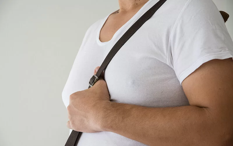 Unter einem engen weißen T-Shirt zeichnen sich bei einem jungen Mann deutlich vergrößerte Männerbrüste ab.