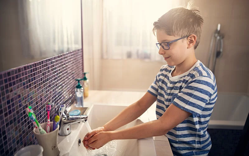 Ein Junge im Grundschulalter wäscht sich im Badezimmer am Waschbecken die Hände mit Seife.