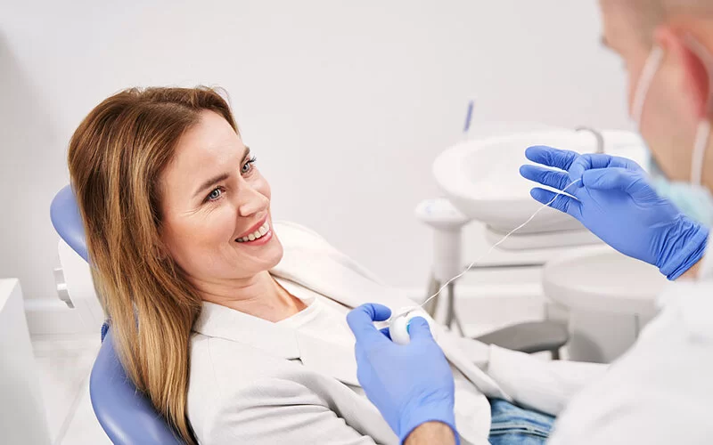 Ein Zahnarzt zeigt einer Patientin, wie sie Zahnseide richtig anwendet, um Parodontitis vorzubeugen.