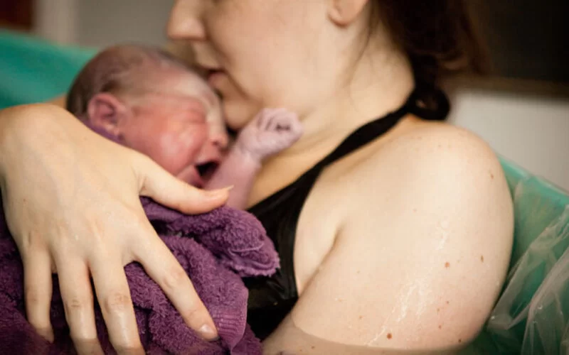 Junge Mutter hält ihr Neugeborenes nach einer Wassergeburt im Arm.