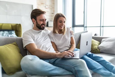 Ein junges Paares sitzt mit einem Laptop auf der Couch.
