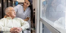 Eine weibliche Pflegefachperson fährt einen Patienten im Rollstuhl durch den Flur.