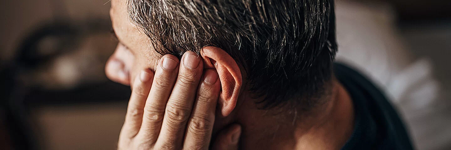 Mann hält sich das Ohr, weil er an einem Tinnitus leidet.