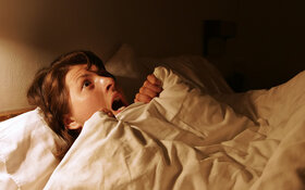 Frau liegt erschrocken im Bett.