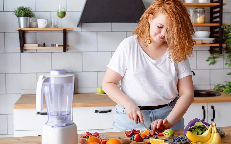 Eine junge Frau schneidet Obst für einen gesunden Smoothie.