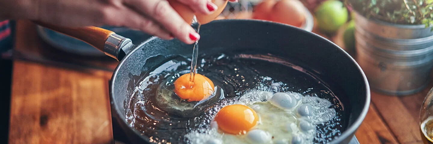 Eine Frau, die eine Eiweißdiät macht, schlägt in einer Pfanne zwei Eier auf.