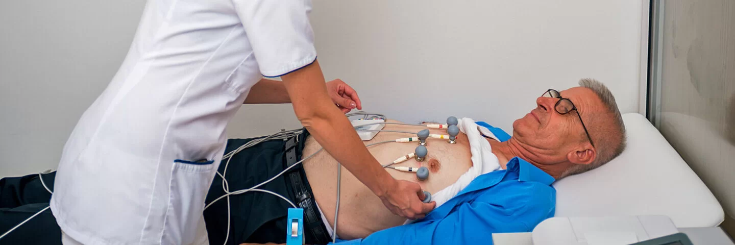 Medizinische Fachangstellte legt einem älteren Patienten Elektroden für ein EKG an.