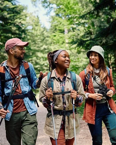 Zwei Frauen und ein Mann wandern mit Rucksäcken und Trekkingstöcken auf einem grünen Waldweg.