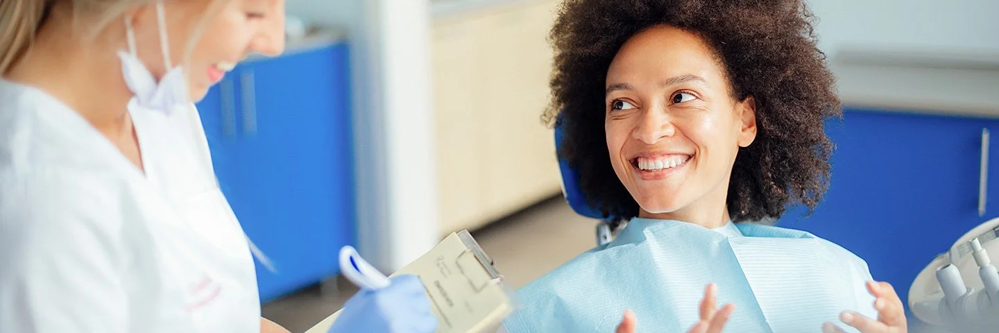 Eine junge Frau ist zur professionellen Zahnreinigung in einer zahnärztlichen Praxis. Eine Zahnazthelferin erklärt ihr den Ablauf der Behandlung.