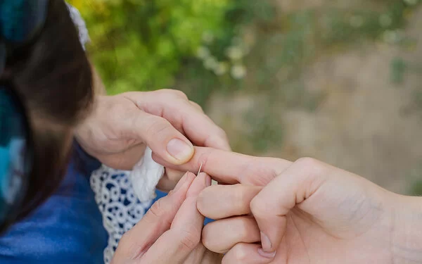 Eine Person entfernt mithilfe einer Nadel bei einem anderen Menschen einen Splitter aus dem rechten Zeigefinger.