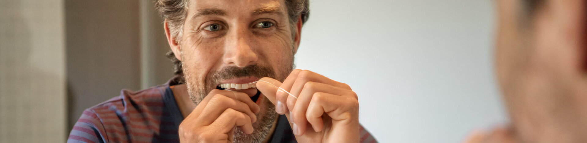 Einem Mann ist die Zahnvorsorge wichtig, er reinigt seine Zahnzwischenräume mit Zahnseide.