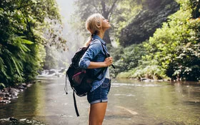 Eine Frau mit Rucksack genießt die handyfreie Zeit an einem Wasserlauf.