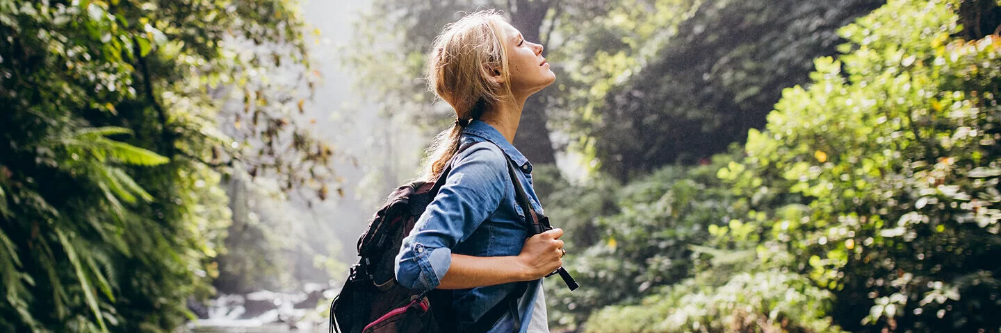 Eine Frau mit Rucksack genießt die handyfreie Zeit an einem Wasserlauf.