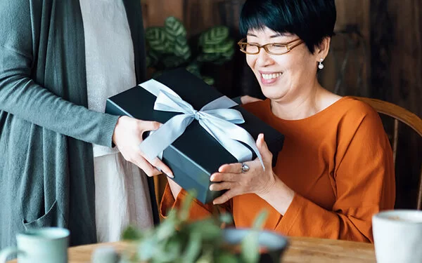 Eine Tochter schenkt ihrer Mutter ein Geschenk mit schönem Geschenkband, das man wiederverwenden kann.