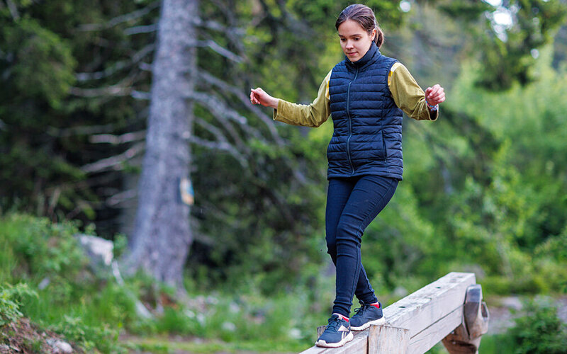 Eine Teenagerin balanciert als Parkour-Übung auf einem Holzbalken im Wald.