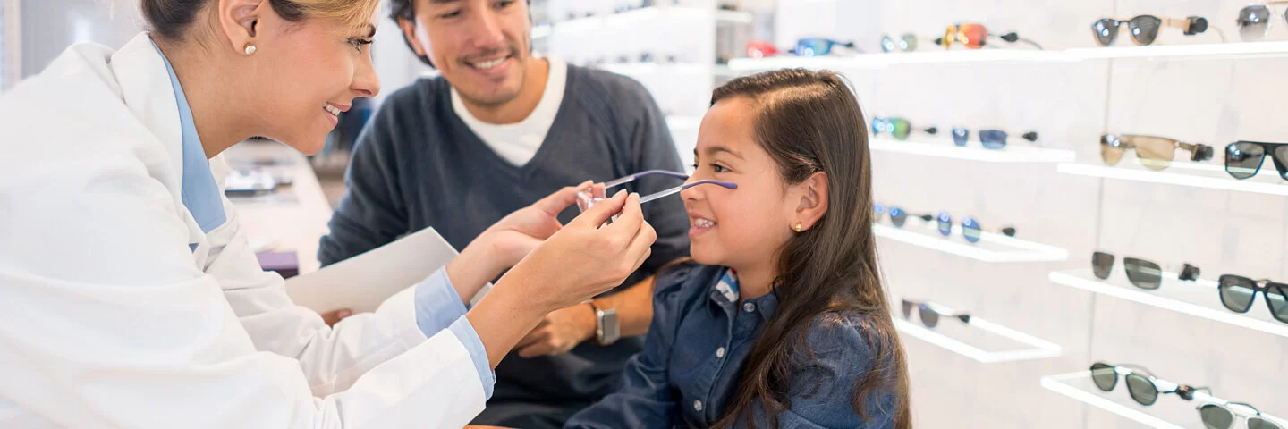 Eine Optikerin setzt einem Mädchen eine Brille auf, damit ihre Sehkraft verbessert werden kann.