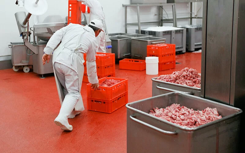 In einer Fleischfabrik schiebt ein Arbeiter rote Plastikkisten mit Fleischresten durch die Halle.